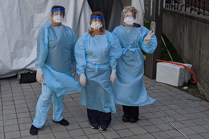 Three nurses wave to camera while wearing medical protective gear