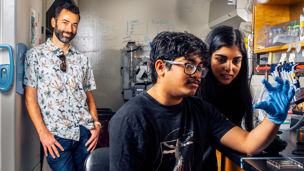 Alex Shalek standing in his lab with two students working in the foreground