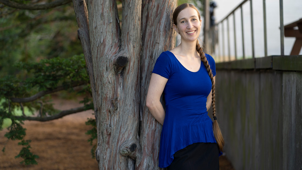Portriat of Emma Gibson, in blue, leaning against a tree on MIT campus