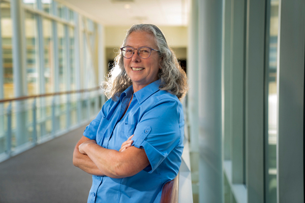 Mary Ellen Zurko indoors leaning on rail with windows in background