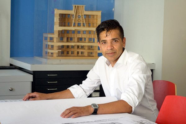 Atif Qadir sitting at a desk in front of wooden model of a building