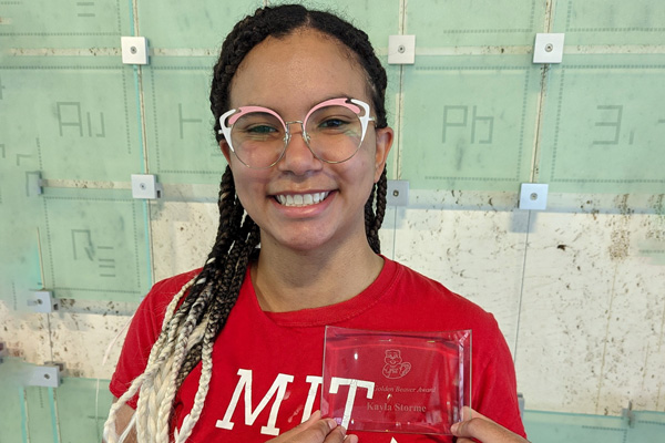 Photo of Kayla Storme wearing an MIT shirt and holding a glass award with her name on it