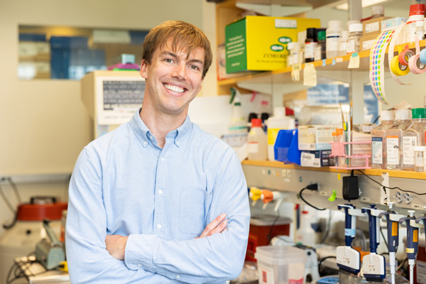 Mitch Murdock smiles in the lab, with shelves and a table filled with colorful equipment and supplies.