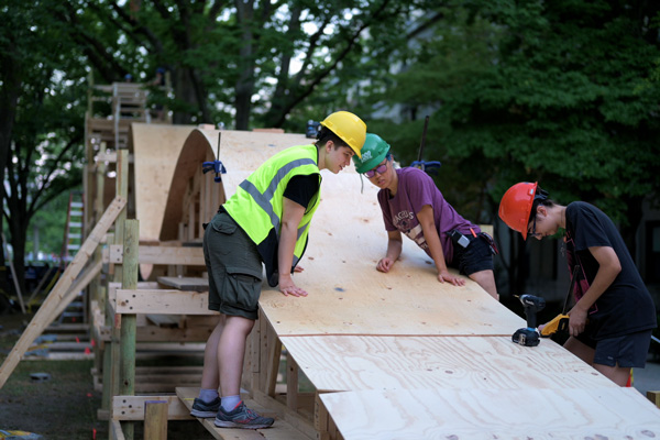 3 students in hard hats and protective gear examine a wood ramp for a roller coast at East Campus