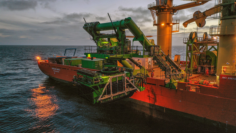 Gigantic arms of an orange and green ship are about to place the smaller green Patania II in the ocean.