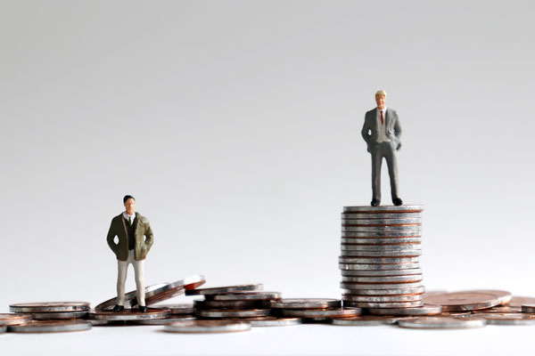 2 plastic toy men, one on pile of a few coins and the other wearing a suit and standing on a tower of coins