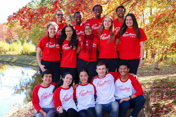Group photo of 14 members of the Chorallaries outside with yellow and orange trees in background.