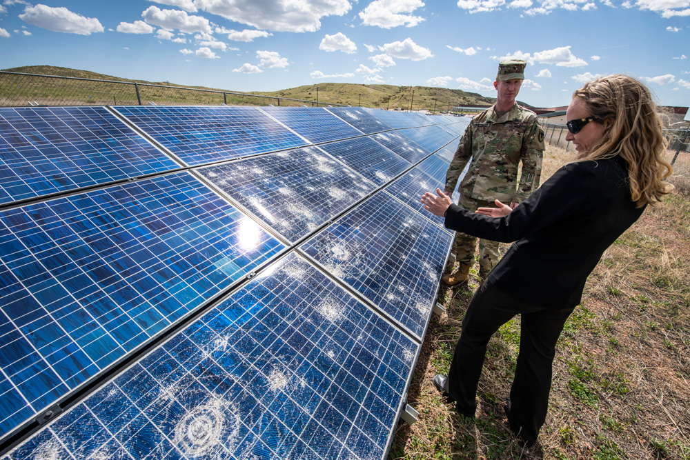 Kate Anderson and man in army camouflage inspect solar panels outside