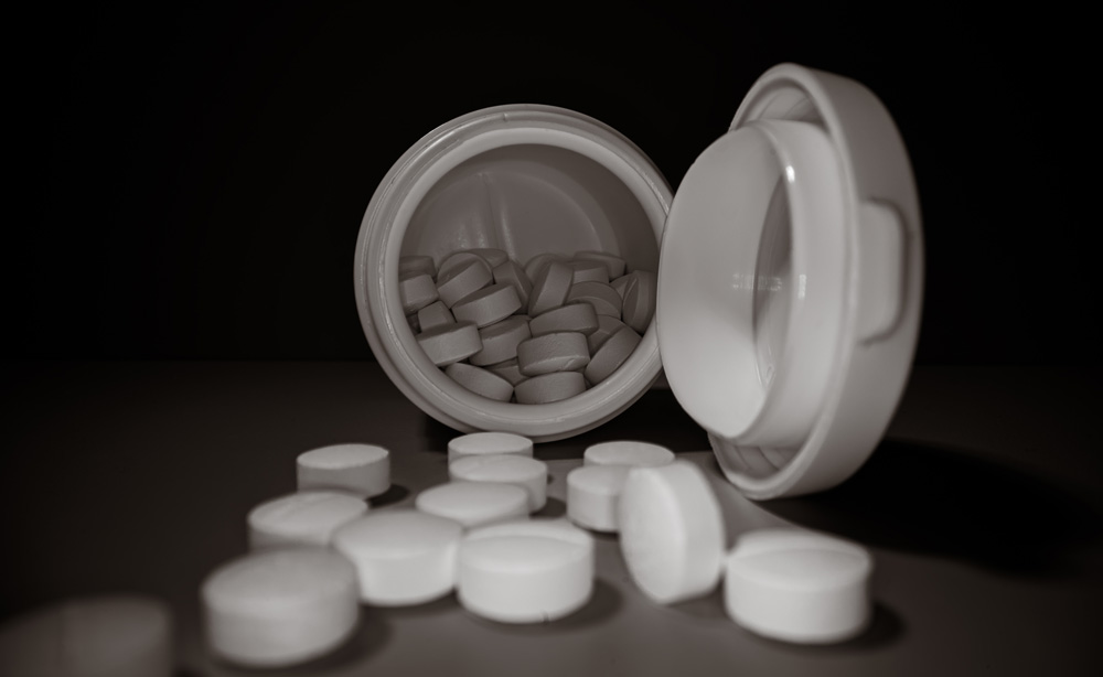 White pills in an open container on black background