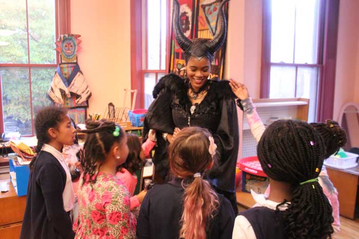 Netia McCray dressed as the witch Maleficent in order to teach Boston elementary school students, pictured here in classroom together, about 3D printing molds for caramel apples for Halloween.