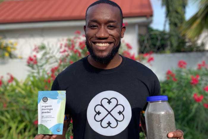 Kwami Williams smiles and holds 2 packaged morigna products