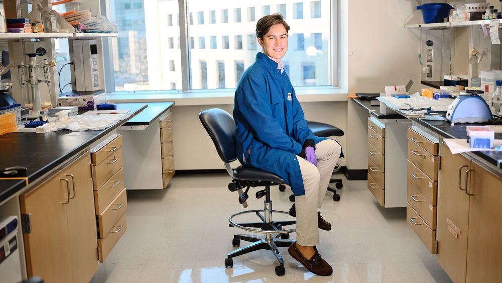 Julian Zulueta sits on a chair in a lab with a large window in background.