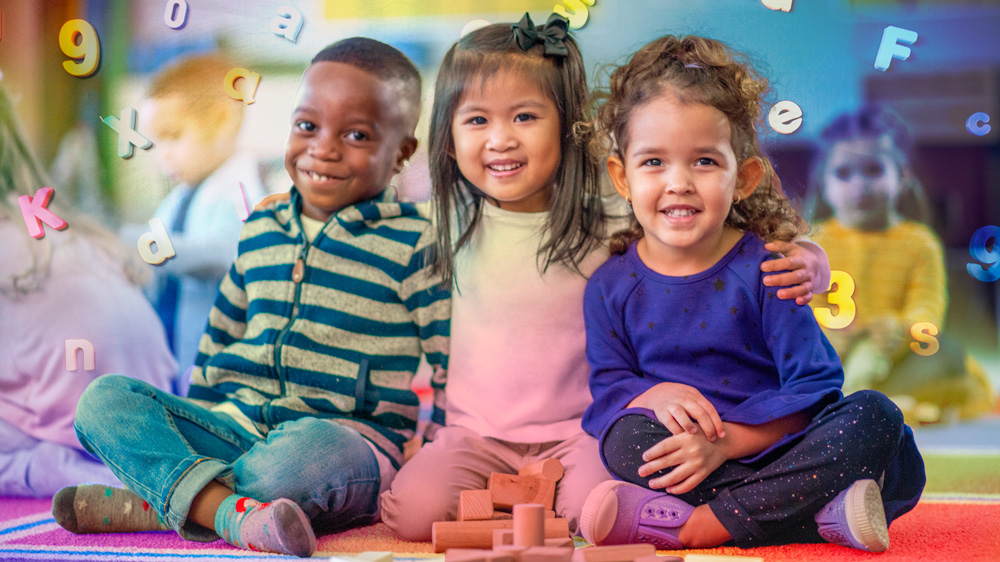 3 smiling preschoolers sit down for a group photo inside a classroom. Letters and numbers swirl around the colorful air.  