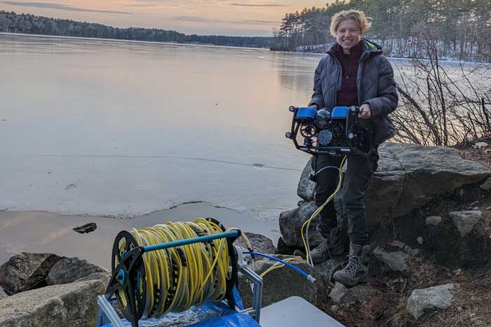 Sylas Horowitz at edge of lake with remotely operated vehicle and lots of yellow cable