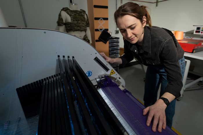 A person inspects a unique loom-like fabric printer, brushing their hand over the threads in this fish-eye lens photo