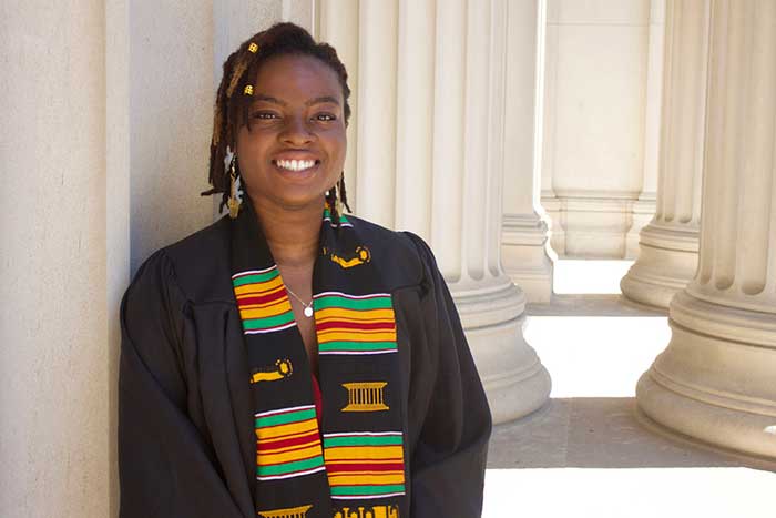 Stacy Godfreey-Igwe poses in front of columns on the MIT campus, wearing her graduation robe and a kente stole.