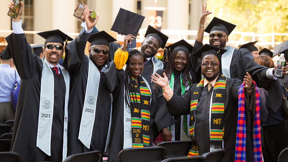 A group of 2023 graduates smile at the camera at Killian Court