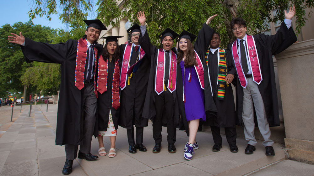 A group of graduates pose and cheer outside near the steps of Lobby 7