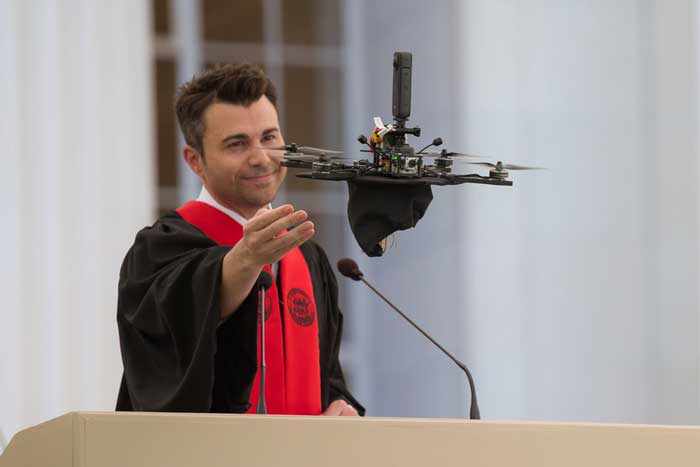 Mark Rober gestures at a drone flying away with his grad cap
