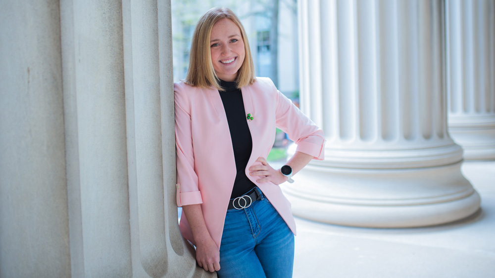 Cunningham wears pink jacket and jeans, and leans against an MIT pillar with one hand on her hip, outdoors.