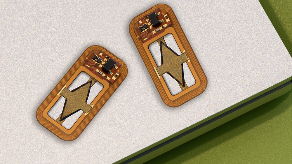 Two tiny rectangular devices have curved edges. The devices are orange-yellow and are made of a circuit board and soldered pieces, including a diamond-shaped piece of material in the middle.