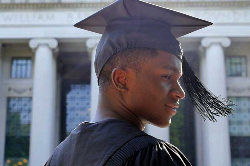 Video still of "Brief Tender Light" shows an MIT student in graduation robes and hat in front of MIT columns