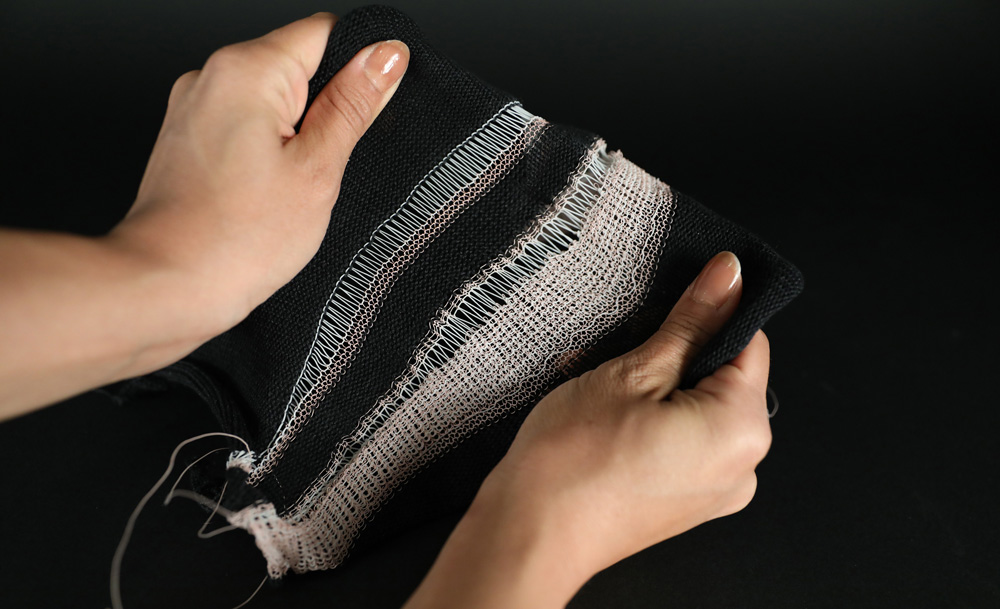 2 hands pull and stretch a piece of black and white fabric that has been sewn using the new fiber.