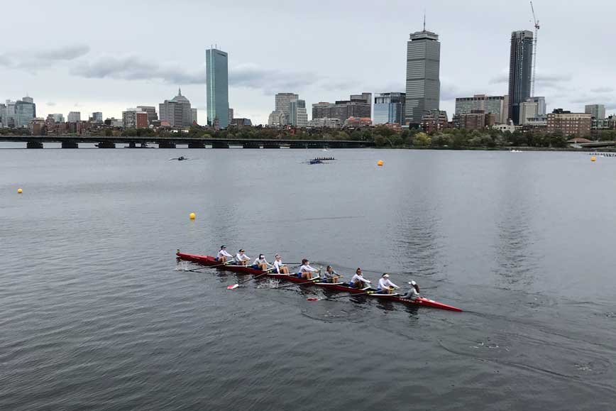 rowing team on calm water with Boston skyline in background