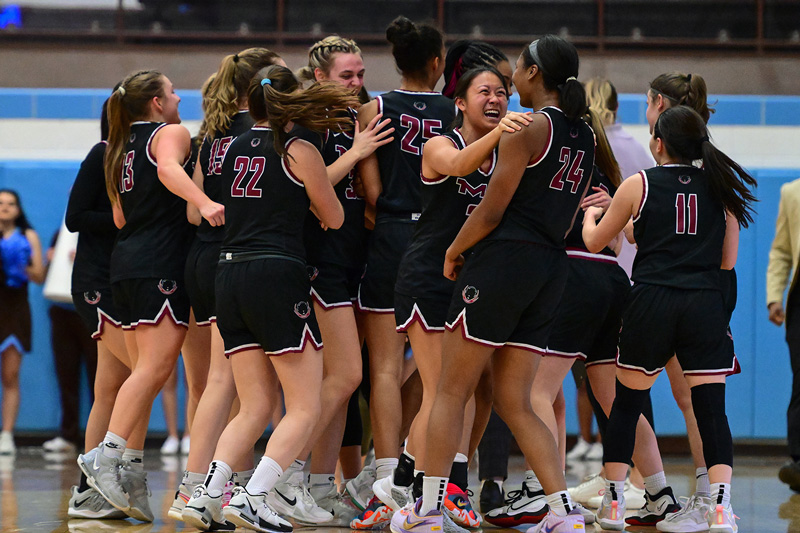 About 15 members of the MIT Women's Basketball team cheer and embrace in a large huddle