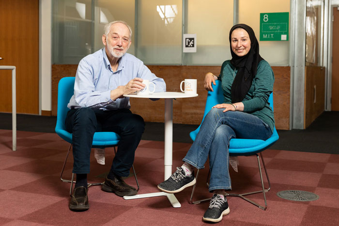 Professor Peter Szolovits, left, and Professor Marzyeh Ghassemi sit together at a small table with coffee mugs inside an MIT building.