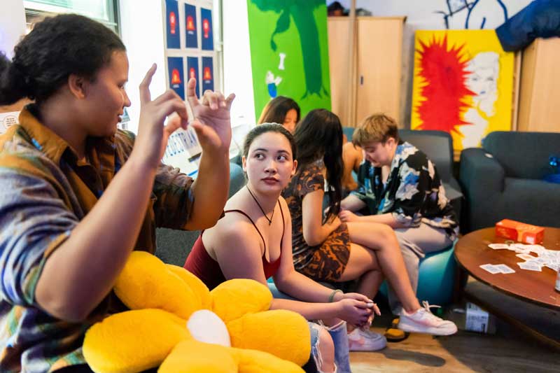 People sit on a couch and exercise ball in a colorful room. Kaylie Cornelius, left, gestures with their hands while Kyna McGill looks on.
