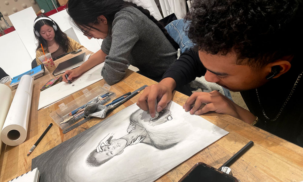 Student Charles Williams draws in an art class, with two students in the background.