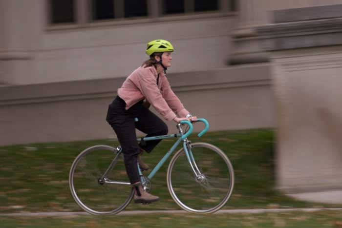 Bianca Champenois rides their bike on campus, with blurry background