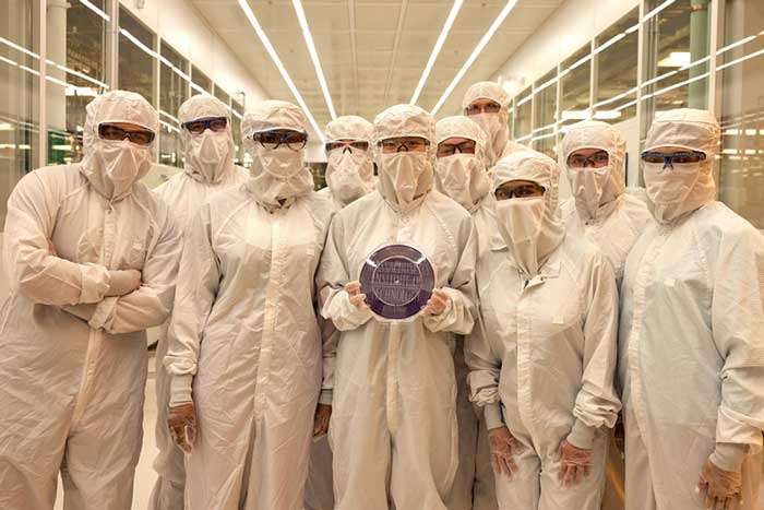 About 8 people in the Nano lab, wearing full-body clean suits, show off a wafer.