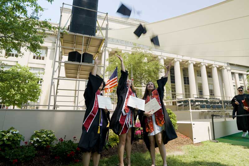 3 recent graduates throw their grad hats in the air