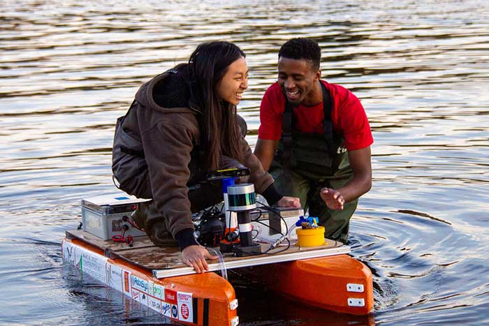 Audrey Chen (left) and Herbie Turner '23 test the durability of their small DIY boat in the Charles River. 