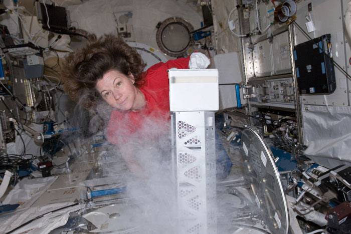 In zero gravity, Cady Coleman poses for a photo with a white canister with icy gas.