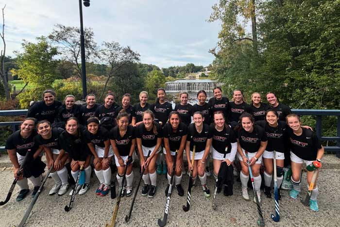 About 25 field hockey teammates pose outside in front of a dam