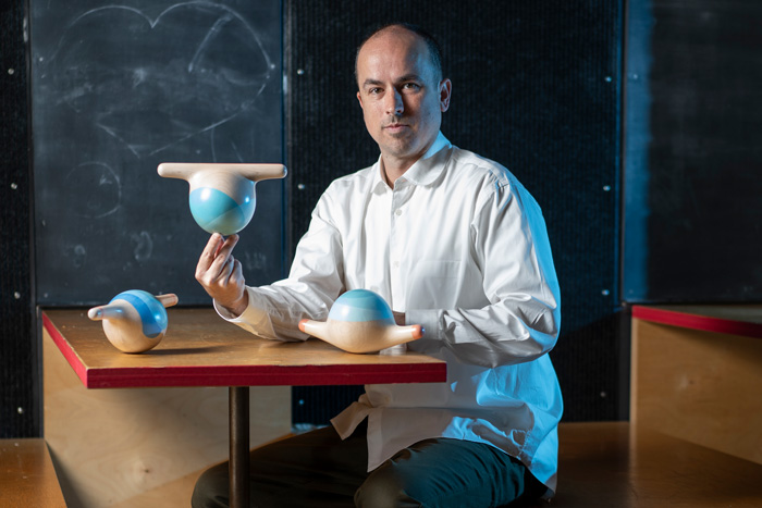 Brandon Clifford sits at a table with 3 bulbous wooden sculptures called "Wobbles"