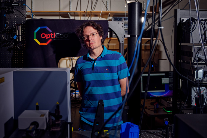 Riccardo Comin stands in the lab filled with cables and large equipment