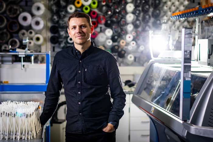 Skylar Tibbits in a lab with colorful spools in background