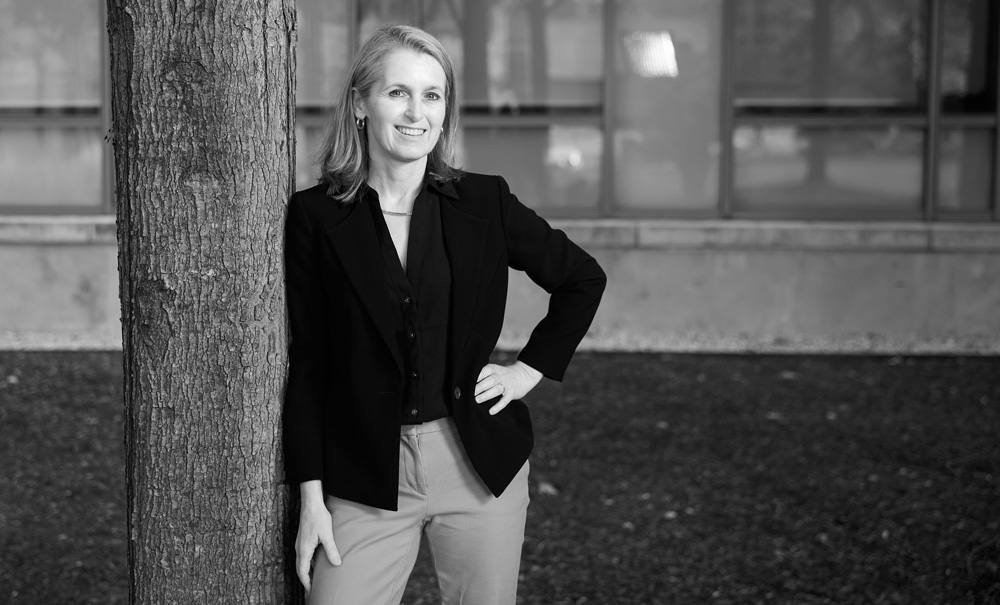 Black-and-white photo of Catherine Wolfram outside learning against tree