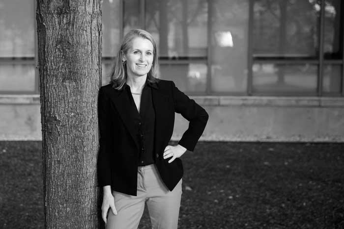 Black-and-white photo of Catherine Wolfram outside learning against tree