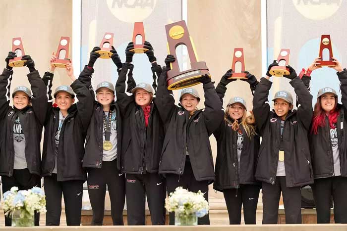 About 9 teammates raise their hands and hold trophies