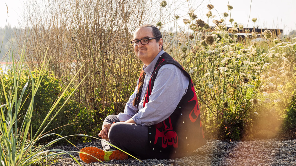 Anthony Jones sits outside on the ground with grasses