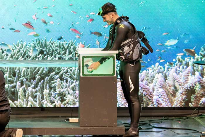 a scuba diver on stage has hands inside an aquarium