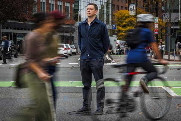 Sevtsuk stands in a crosswalk, as blurry travelers go by