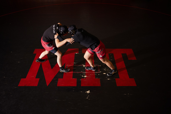 2 wrestlers grapple, and the mat says "MIT."