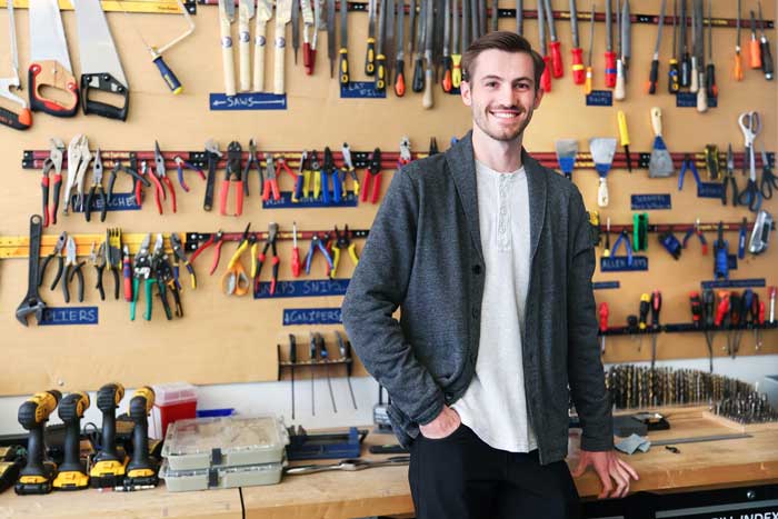 Zane Schemmer in front of a workbench, with various tools on a wall-mounted pegboard.