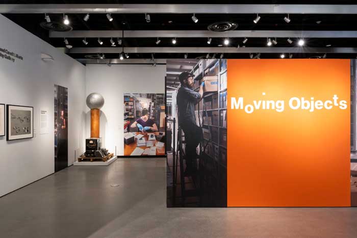 A museum exhibit has a big orange poster saying "Moving Objects."